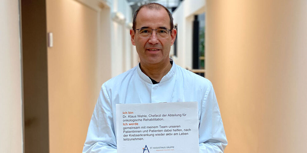 Dr. Wehle hält ein Schild mit "Ich bin... und ich werde..." in die Kamera.